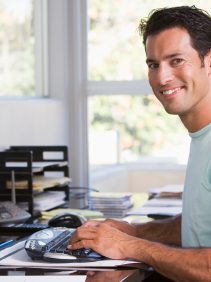 Man in home office using computer and smiling
